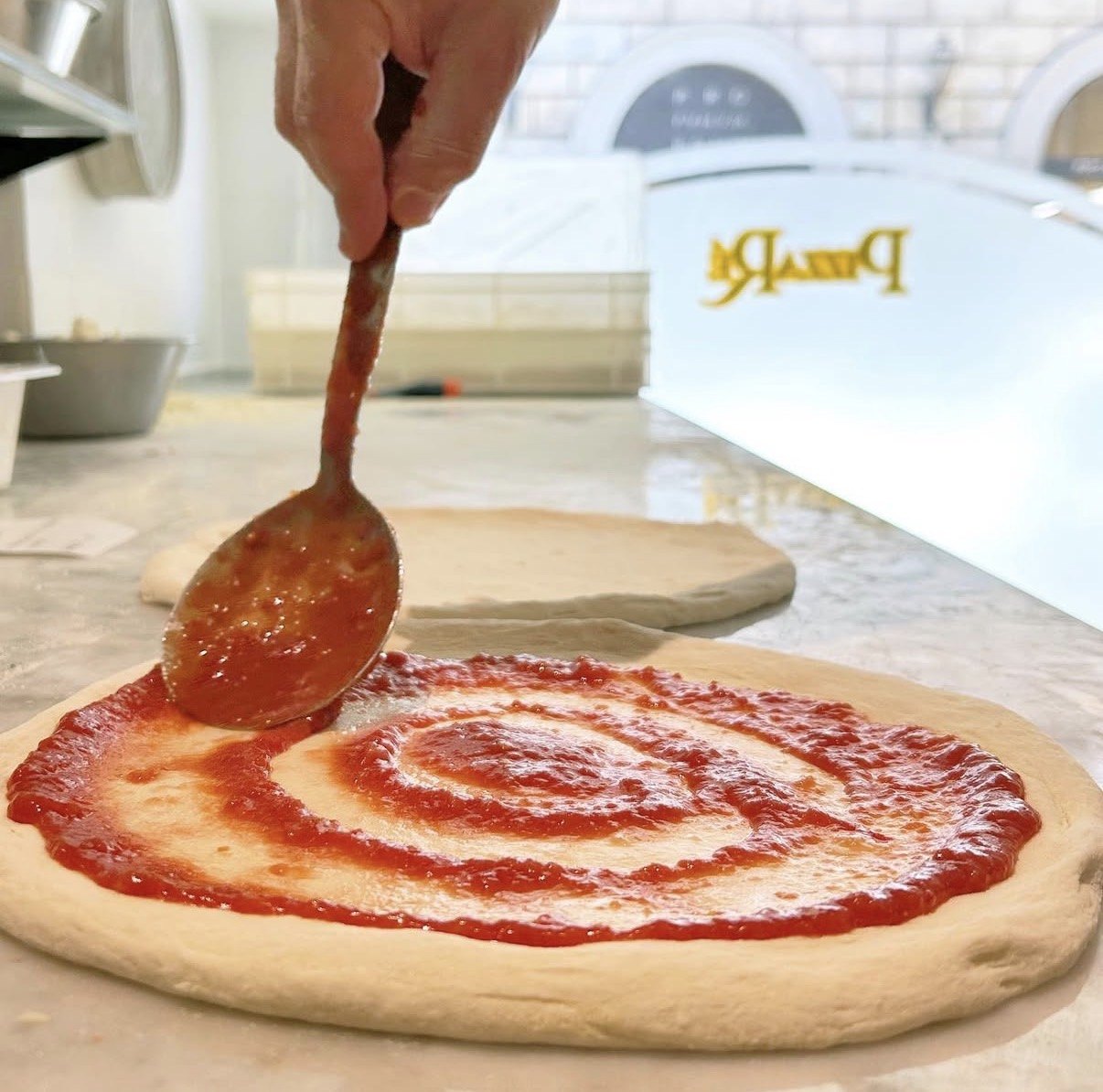 Pizzaiolo che stende la salsa di pomodoro sul disco di impasto